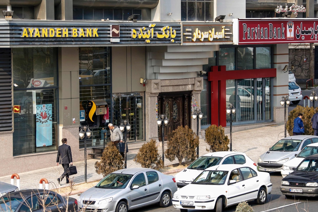 Iranians walk past an Ayandeh Bank facility in 2017.